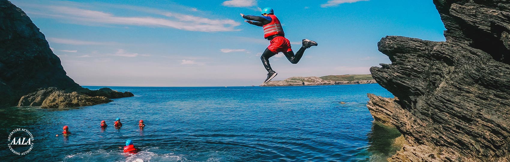 Woman cliff jumping from a high cliff into sea at Porth Dafarch